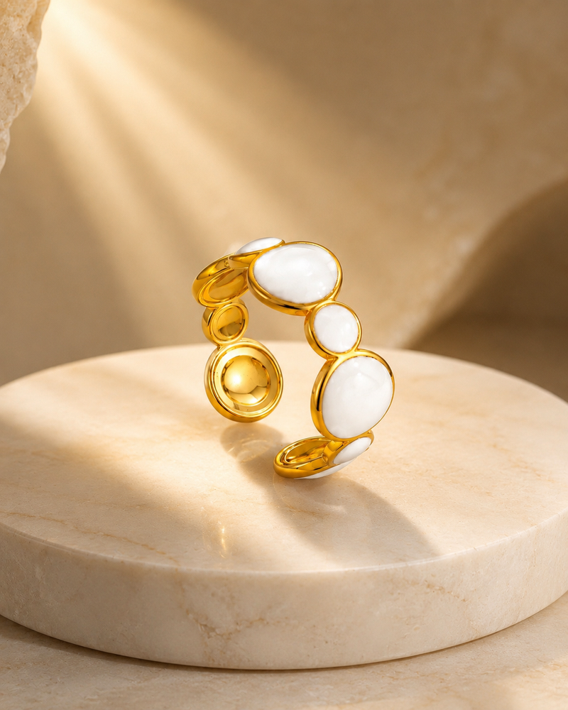 Anillo EDÉN de NYXIDIE: anillo abierto en acabado oro de 18K con cabujones blancos, sobre pedestal de mármol.